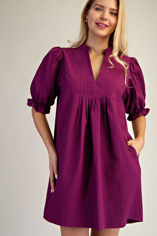 Lyla Puff Sleeve Dress in deep purple with V-neckline, puff sleeves, gathered pleats, pockets. Available in sizes XS–XL.