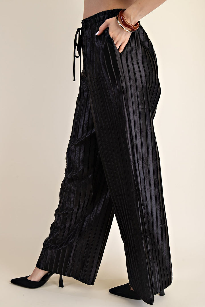 Pitch Flowy Pants: high-waisted, wide-leg black satin with vertical stripes. Available in sizes XS–XL.