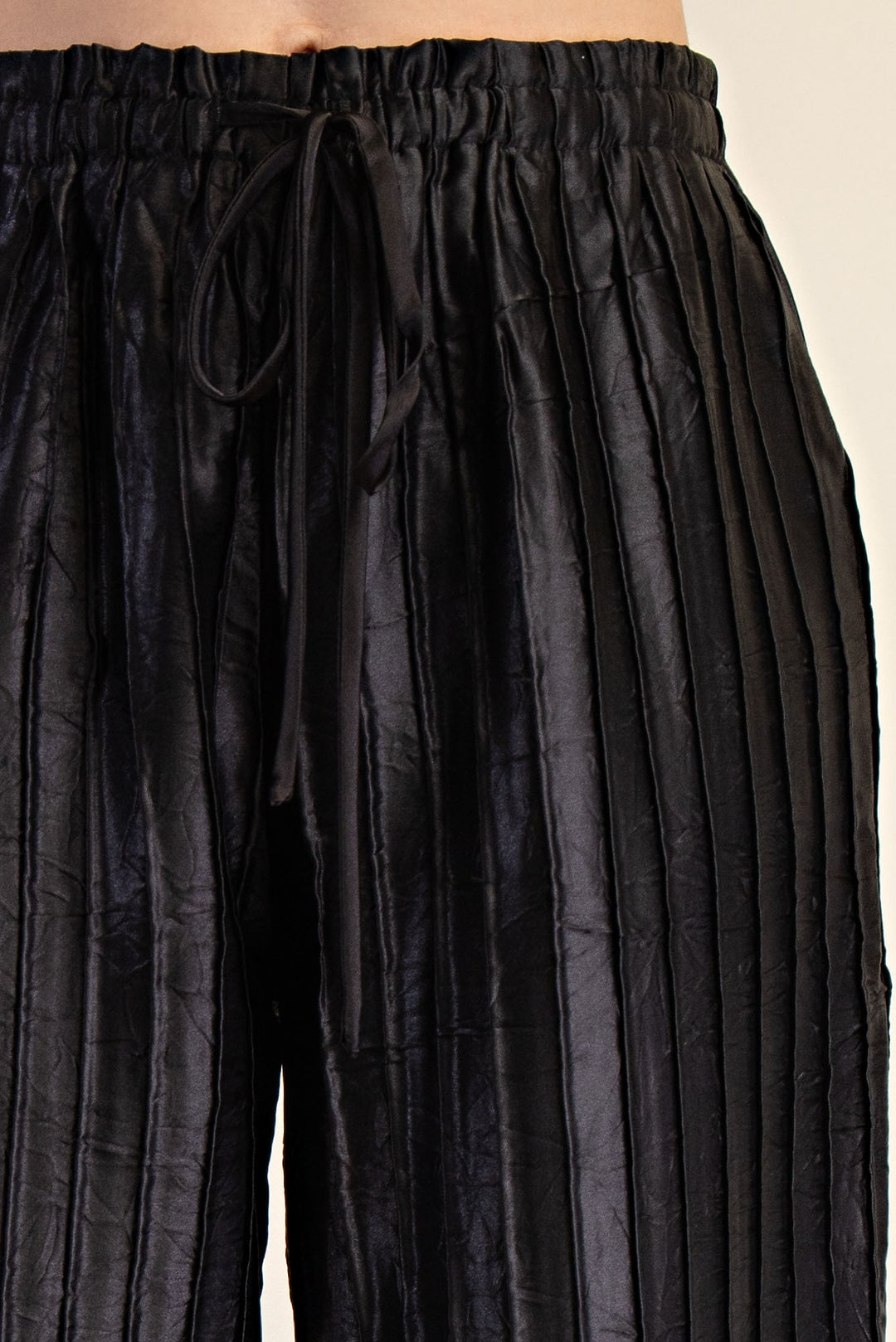 Pitch Flowy Pants: black, pleated, wide-leg, shiny metallic fabric, elastic waistband, front drawstring. Sizes XS–XL.
