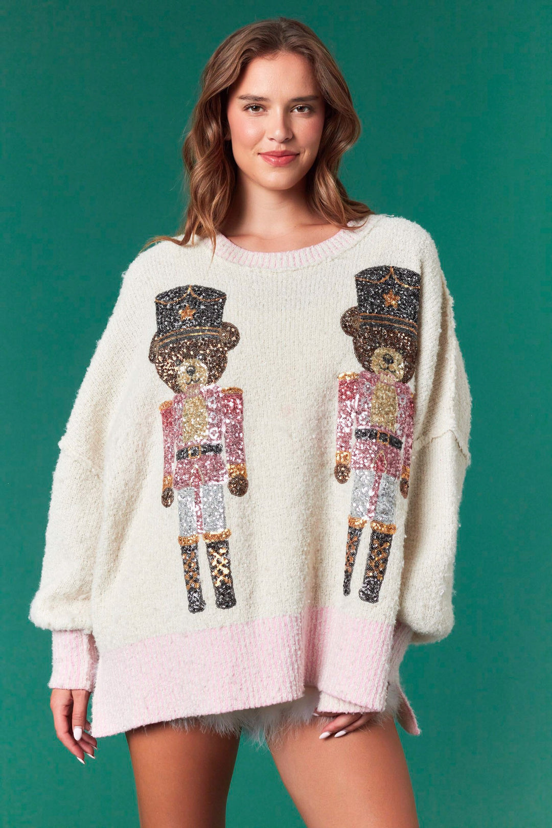 Cream-colored knit sweater featuring two sequined toy soldier bears and pink trim. Available in multiple sizes.