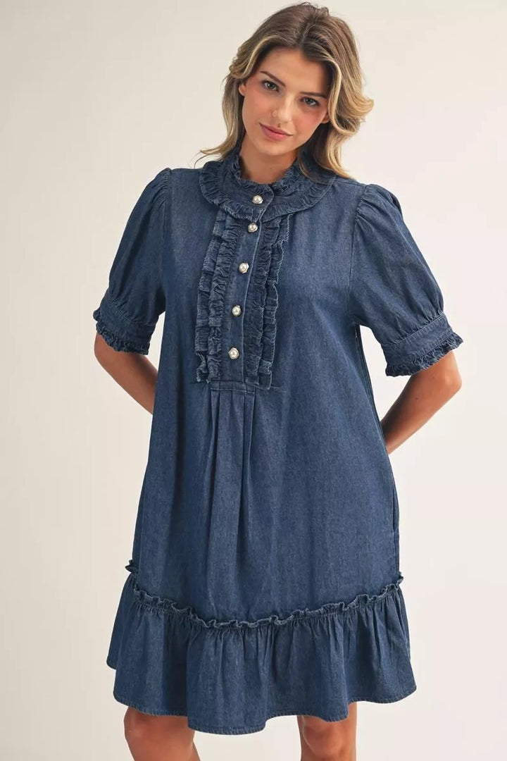 Blue Darcy Ruffle Denim Dress with short puff sleeves, ruffled collar and placket, pearl-style buttons, and ruffled hem in a button-front style. Sizes available.