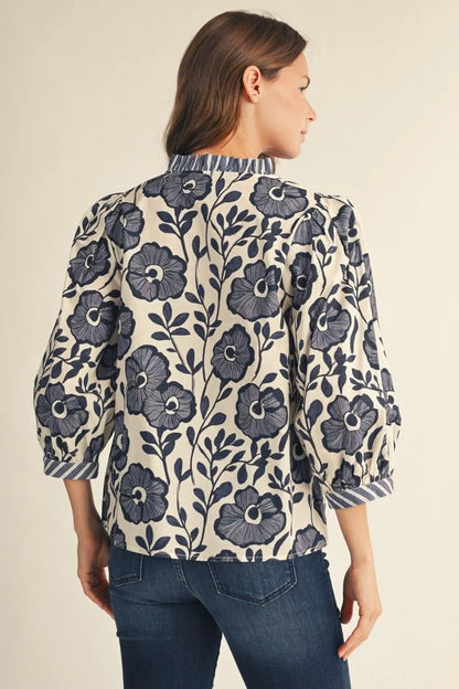 Bonnie Ruffle Floral Blouse in cream featuring bold navy floral prints, ruffled neckline, and puffed sleeves. Available in sizes XS–XL.