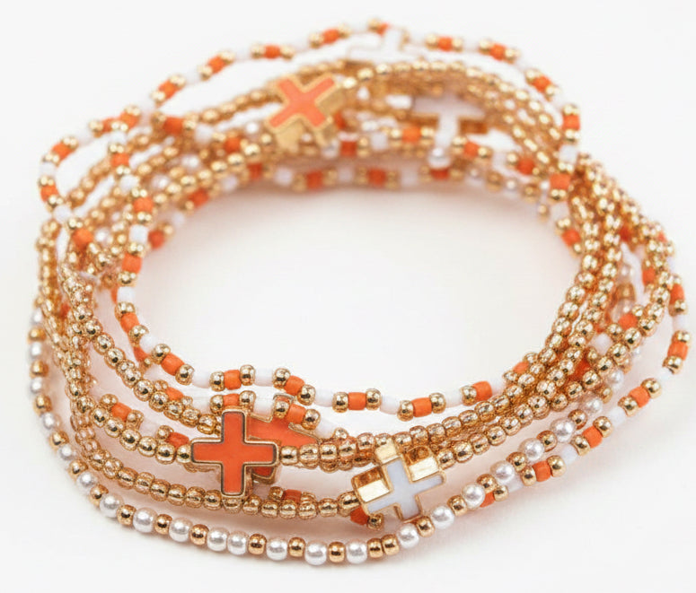 The Irina Orange & White Layered Bracelet features gold, orange, and white beads with cross-shaped charms. Available in multiple sizes.