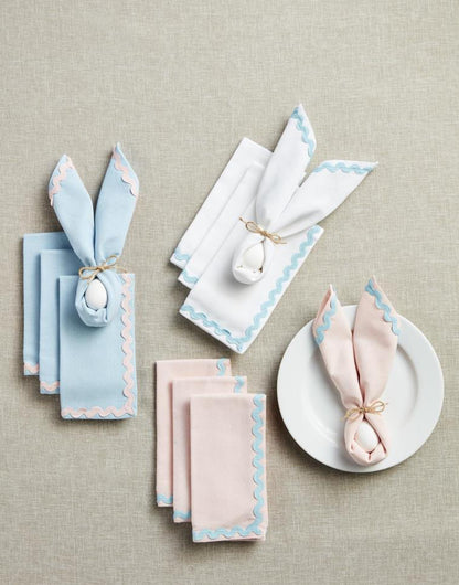 Pastel cotton napkins with ric rac trim, 18" x 18", folded into bunny-ear shapes.