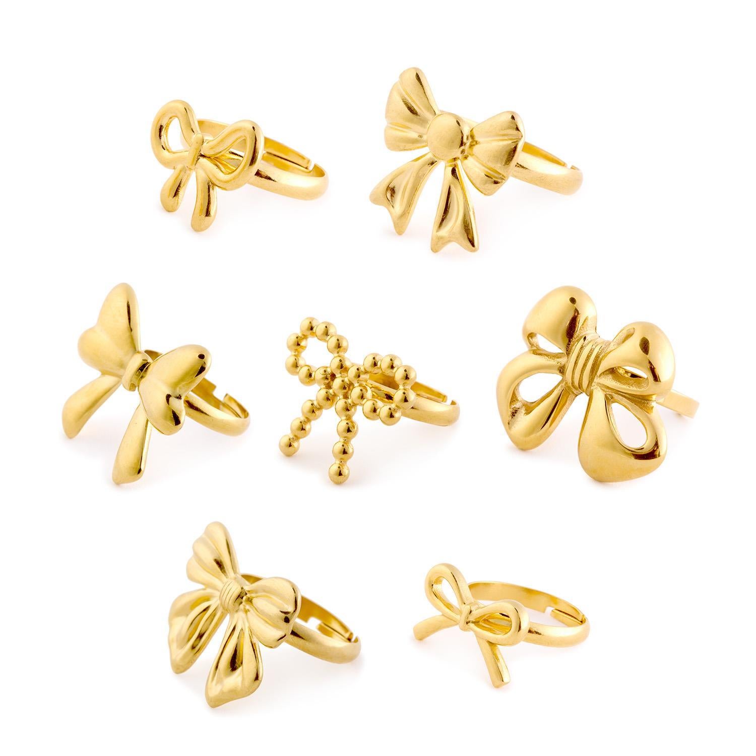 Set of seven gold bow rings, including Forget Me Not and an adjustable ring. Available in sizes 5-9.