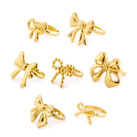 Set of seven gold bow rings, including Forget Me Not and an adjustable ring. Available in sizes 5-9.