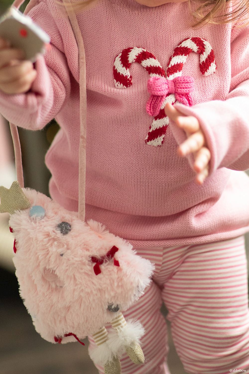 Fluffy pink Christmas tree-shaped plush purse with ribbon details and dangling legs.