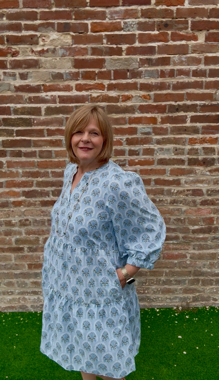 Light blue patterned V-neck Cooper Botanical Blooms Dress with tiered skirt and pockets. Available in sizes XS-XL.