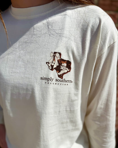 Off-white Texas Animal Print Long Sleeve shirt from Simply Southern Collection with a decorative cow leopard graphic on the chest. Available in sizes S–XXL.