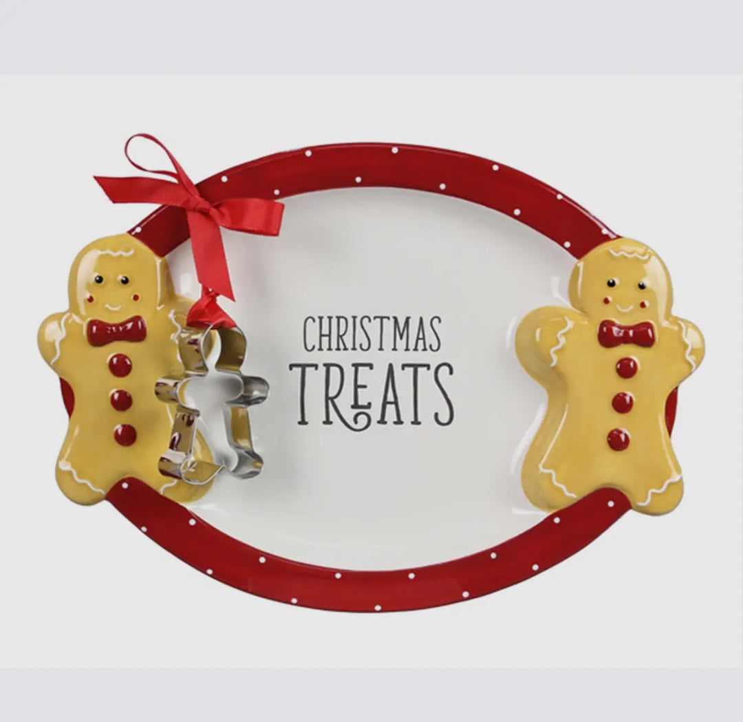 Oval ceramic cocoa and cookie treat platter with a red, white-dotted rim, gingerbread men, “Christmas Treats” inscription, and an attached metal cookie cutter.