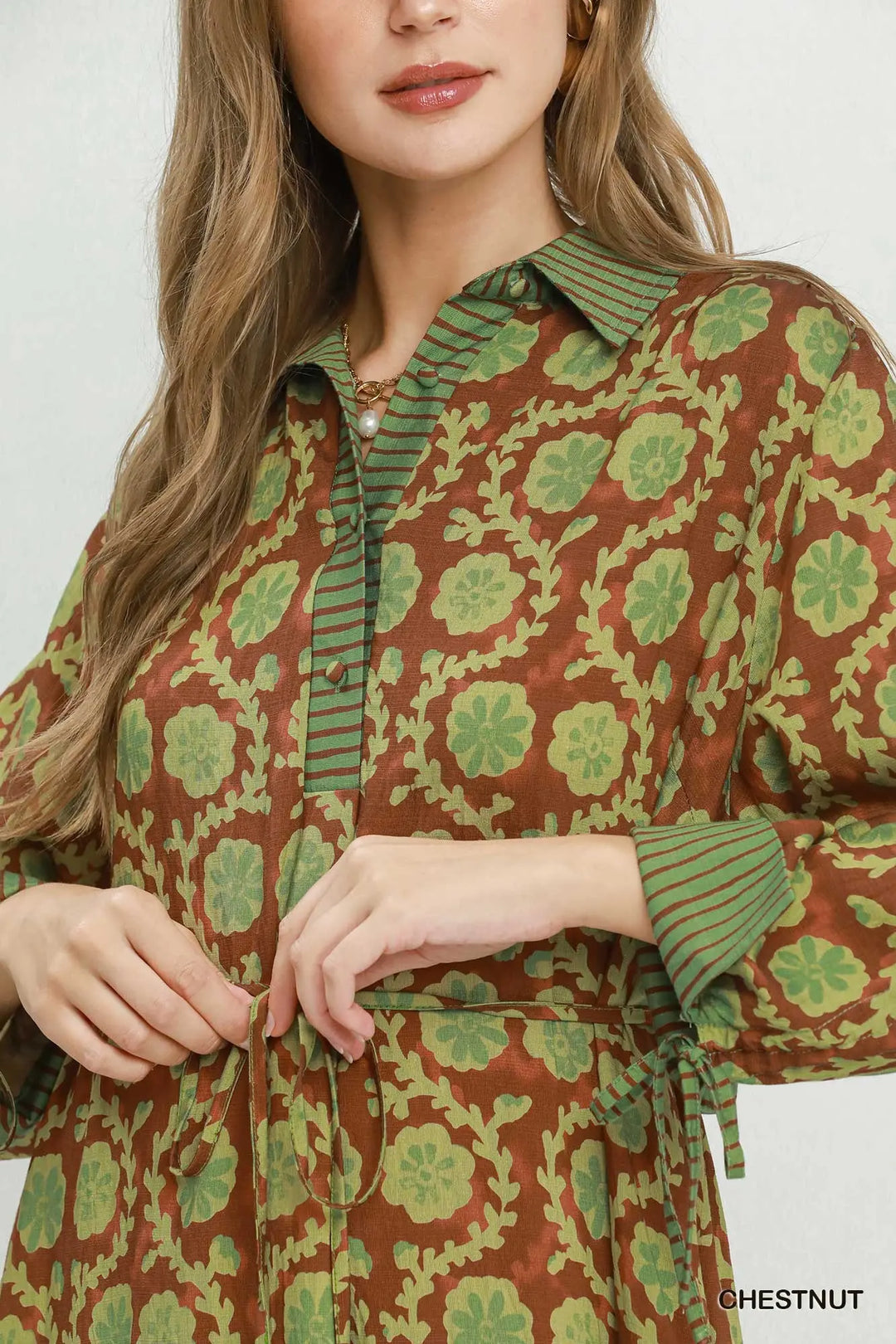 Brown midi dress with green floral pattern, tie waist, button-down front, collar, and striped trim on cuffs and placket. Available in sizes XS-XL.