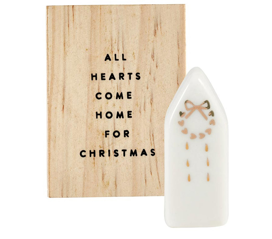 Ceramic figurine pine wood box with “All hearts come home for Christmas” wooden sign and white ceramic house-shaped figurine with gold heart wreath design.