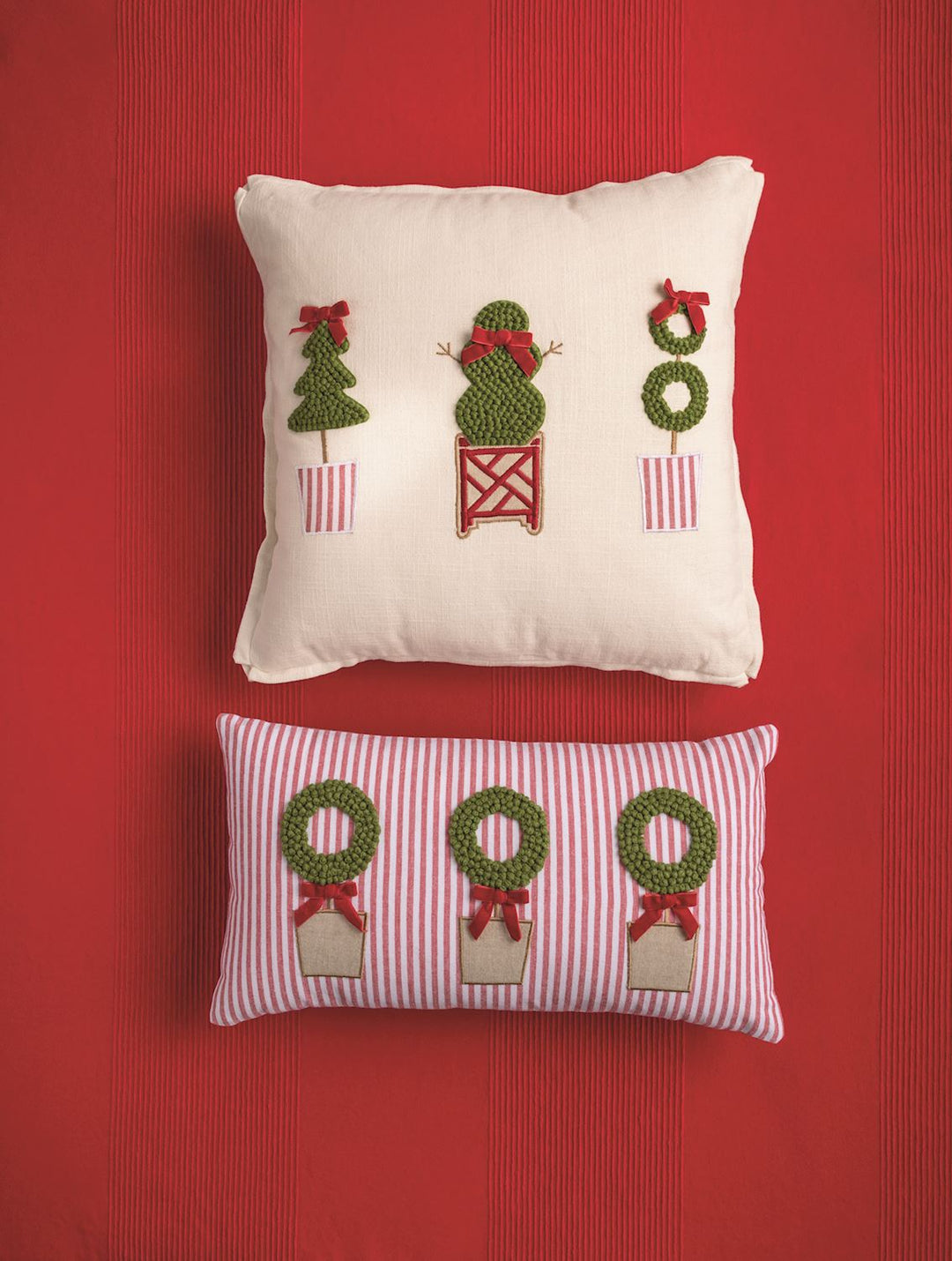 Square holiday throw pillow with three embroidered potted trees and rectangular Lumbar Topiary Holiday Throw Pillow with three embroidered wreaths in planters.