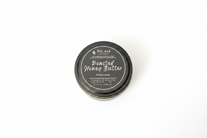 Small round tin labeled "Roasted Honey Butter" Wickless Candle, 5.75 oz size, No. 948, made from coconut soy wax with a black lid featuring white decorative text and product details.