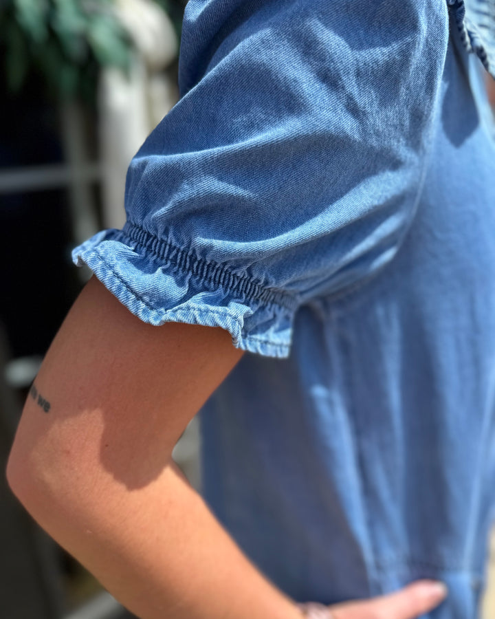 Denim Ruffle Collar Mini Dress in light blue denim with short sleeves and ruffled edges. Available in sizes XS–XL.