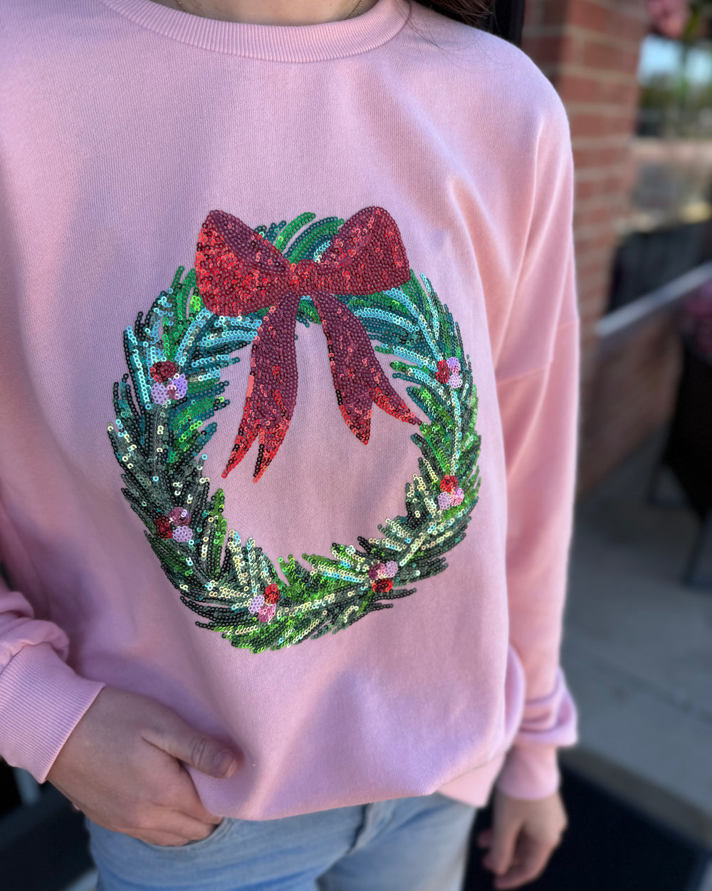Light pink Clara Wreath Sequin Sweatshirt with a sequined Christmas wreath and red bow.