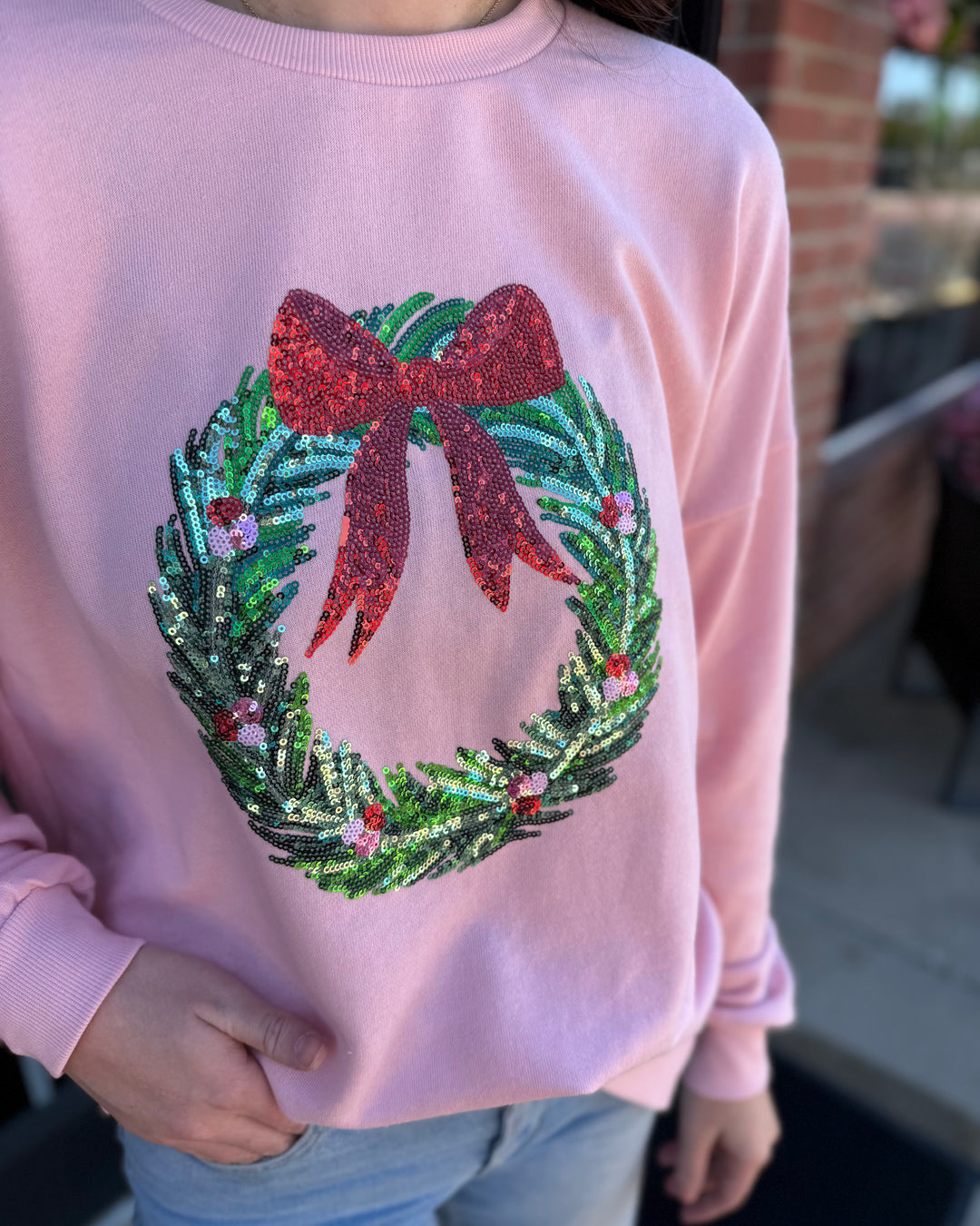 Light pink Clara Wreath Sequin Sweatshirt with a sequined Christmas wreath and red bow.