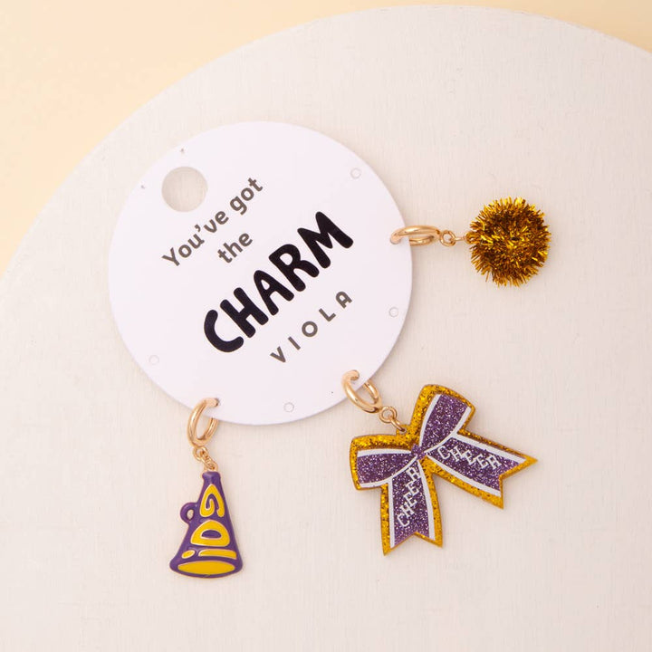 Gold and purple Pom Pom, Megaphone, and Glittered Bow keychain charms on a white card. Sizes: one size only.