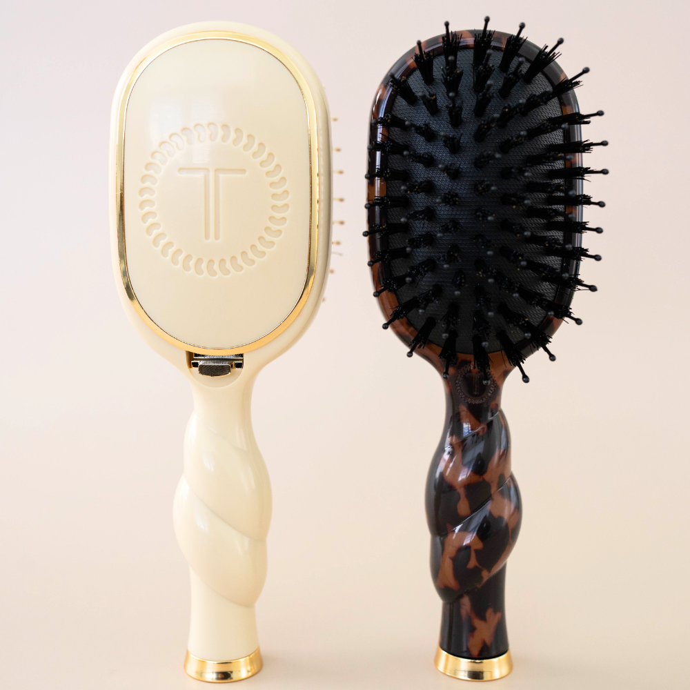 Two Mini Boar Brushes with twisted handles, gold accents, and oval heads—one cream with a logo, one dark brown tortoiseshell with black natural bristles. Available in mini size.