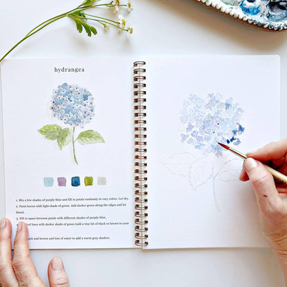 The Flowers Watercolor Workbook, spiral-bound, shows hydrangea painting instructions and color swatches. Sizes: standard only.