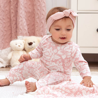 Baby modeling romper and headband sitting up on carpet.