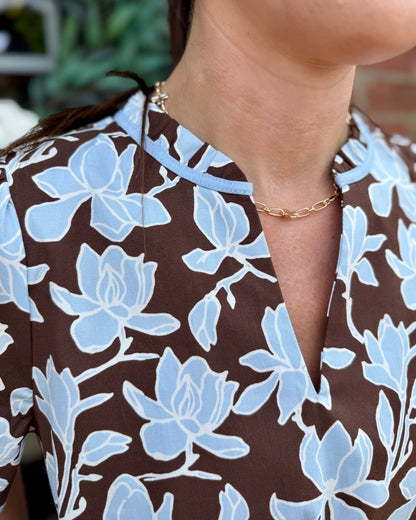 Brown mini dress with light blue floral patterns and delicate light blue trim. Available in sizes XS–XL.