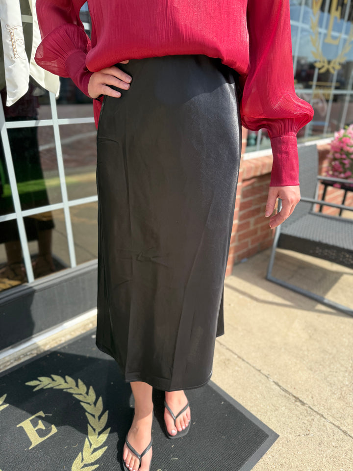 The Glitter Midi Skirt is a long black satin skirt with an elastic waist, available in sizes XS–XL.