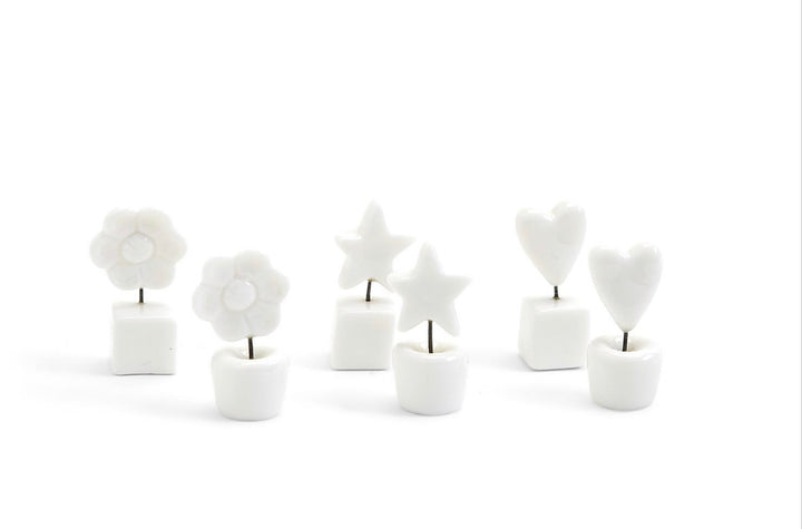 Six small white ceramic holders with metal stems topped by white flowers, stars, or hearts; available in one compact size.
