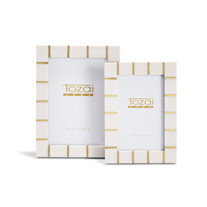 White rectangular resin photo frames with gold horizontal stripes from the Brass Lines collection, available in two sizes. Each frame displays the "Tozai Home" logo and frame dimensions.