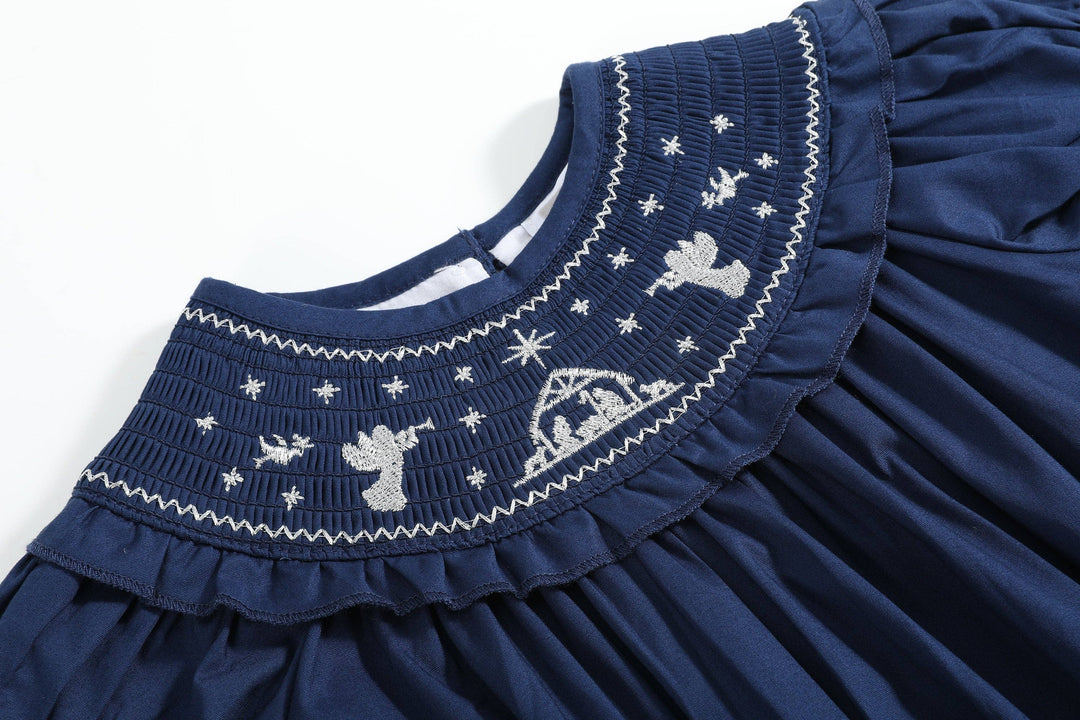 Navy blue romper with smocked collar, white embroidered angels, stars, and nativity scene; available in size 2T.