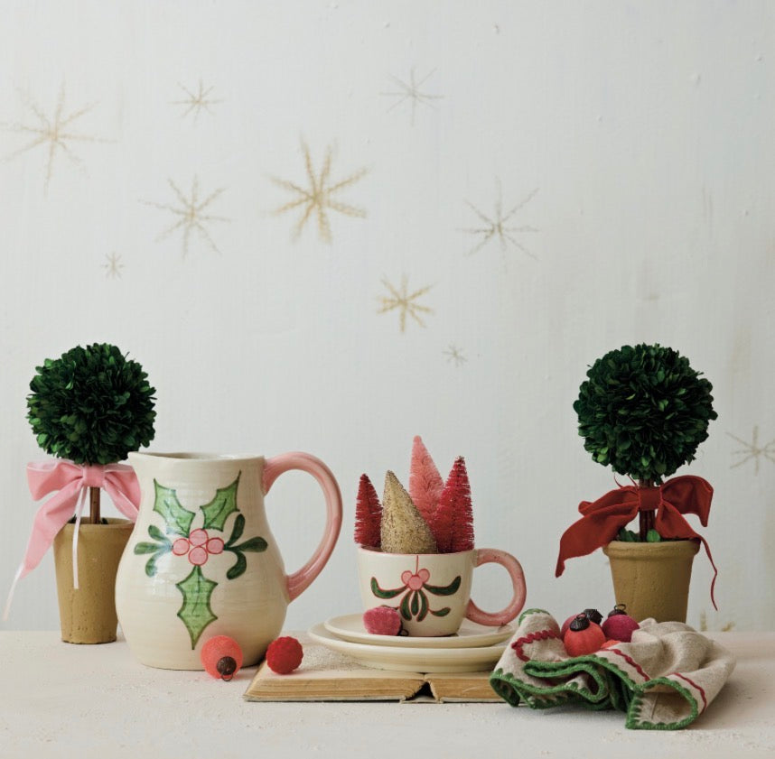 Two small, spherical dried boxwood topiary trees with velvet bows in terra-cotta pots.
