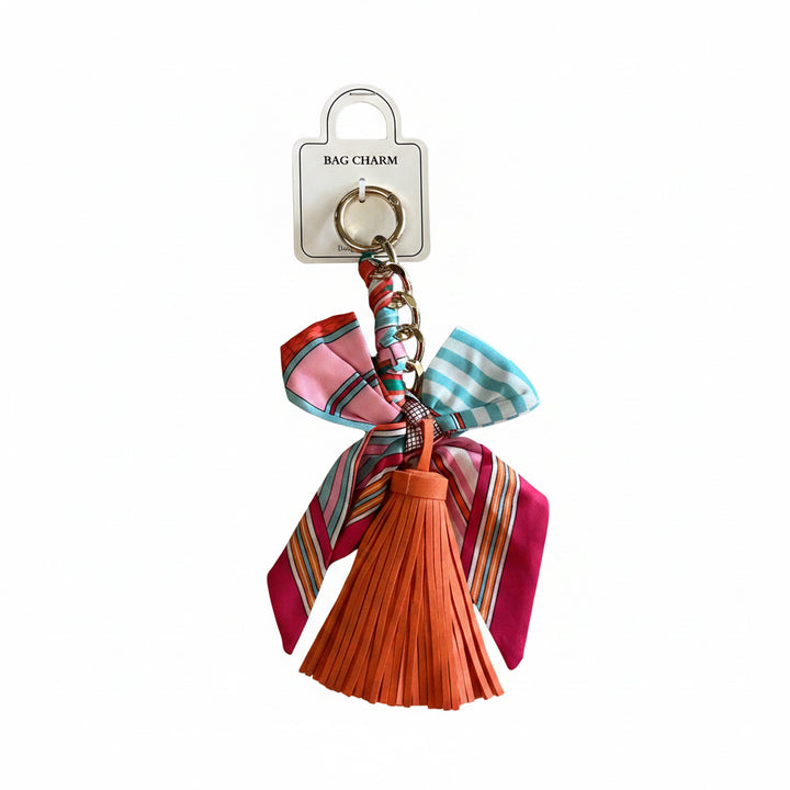 Vibrant orange tassel with pink, blue, and red striped ribbons on a gold-toned ring and a white “BAG CHARM” tag. Available in small and large sizes.