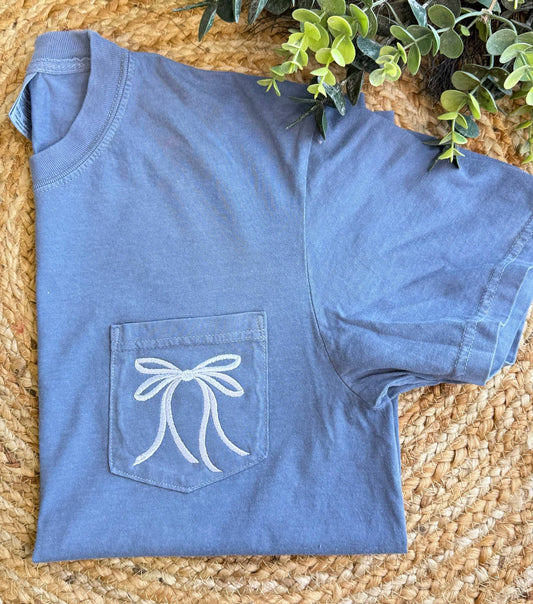 White Bow Comfort Color T-Shirt, washed blue with white bow on pocket, available in sizes S–XL.