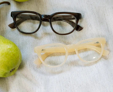 Two Peepers Kitt eyeglasses with lightweight frames, one dark brown and one translucent beige; both offer UV400 protection. Sizes available: small, medium, large.