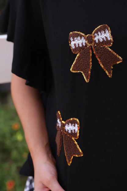 Sideline Sparkle Ruffle Top: black shirt featuring two brown and white sequin bows outlined in gold, one on the chest and one near the waist. Available in sizes XS–XL.
