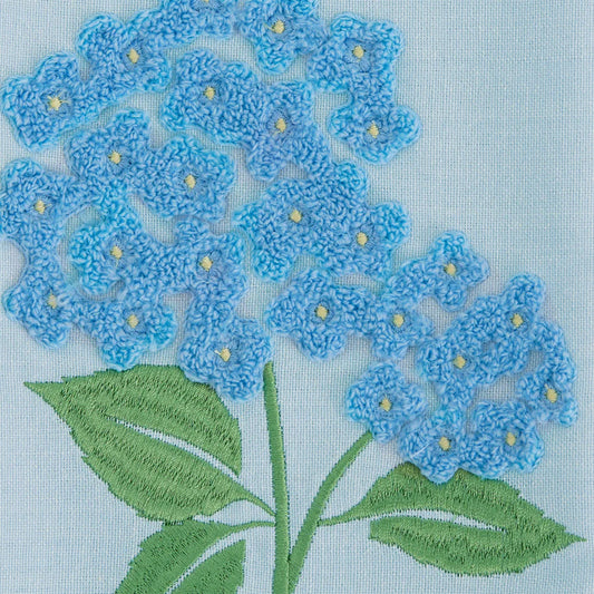 Dishtowel with embroidered blue hydrangea clusters, yellow centers, and green leaves. Available in one standard size.