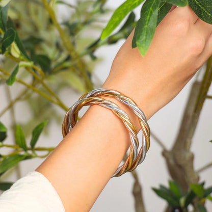 Two intertwined Trilogy All Weather Bangles, one silver and one gold, shown together; available in small, medium, and large sizes.