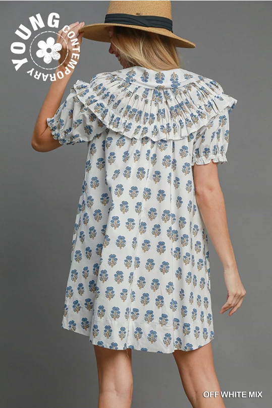 Loose-fitting white cotton mini dress with blue and yellow florals, pleated collar, puff sleeves. Sizes: XS–XL.