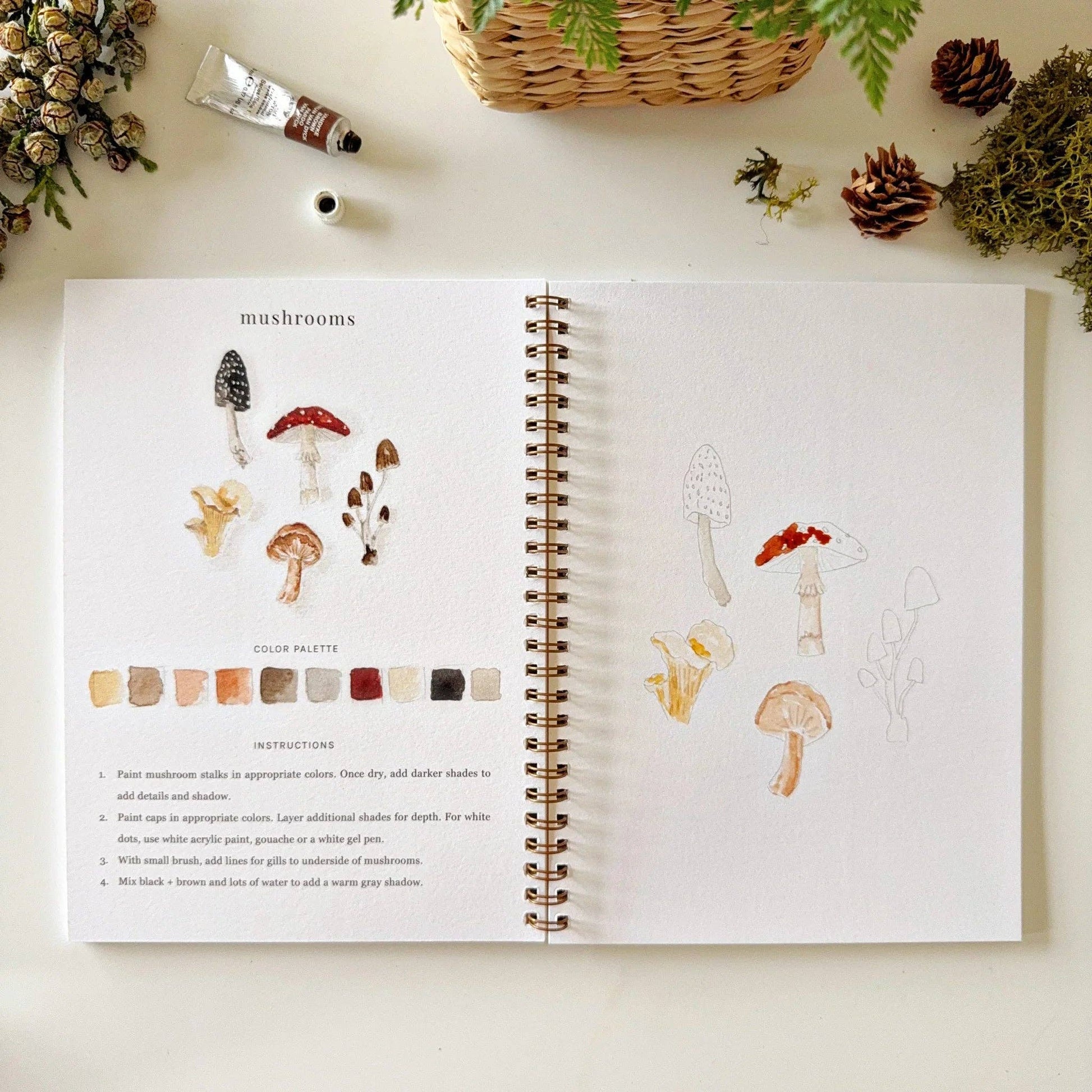 The Woodland Watercolor Workbook is open, showing woodland-themed mushroom illustrations, color palette swatches, and step-by-step painting instructions. Available in standard size.