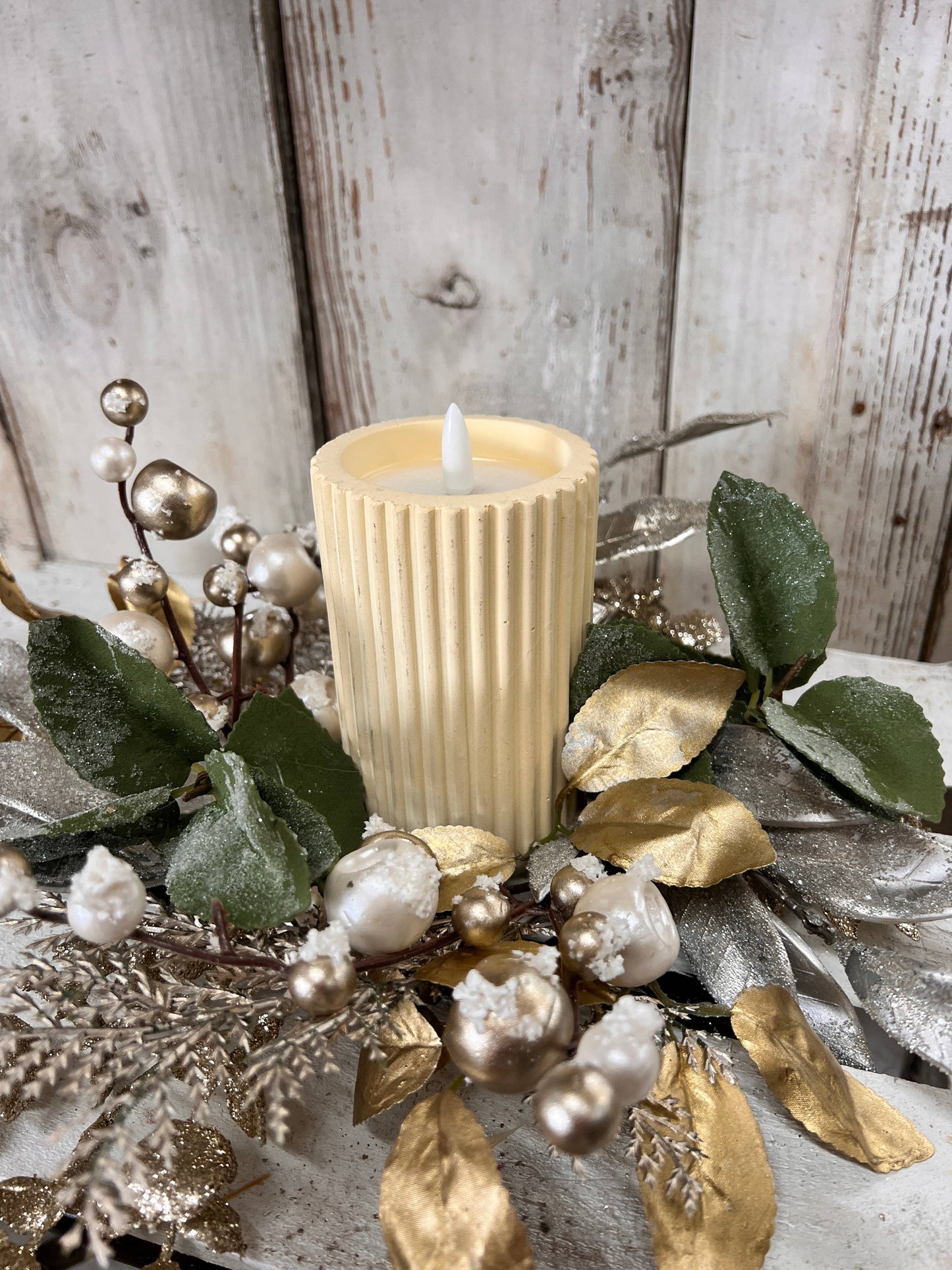 The Glitz And Glamour Candle Ring 4.5in includes a ribbed cream-colored candle with faux greenery, white berries, and gold-silver leaves. Available in 4.5-inch size.