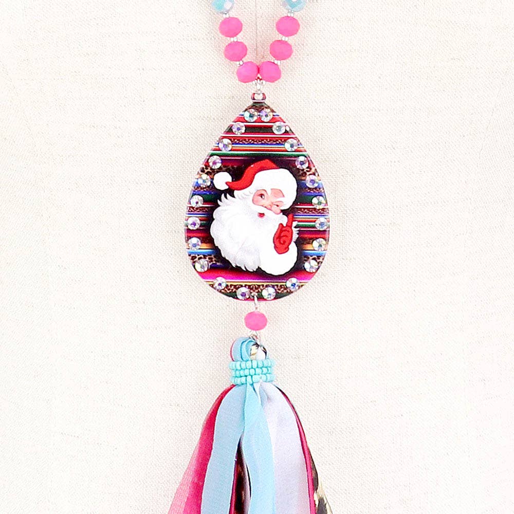 Santa Claus serape teardrop tassel pendant long necklace with rhinestone frame, multi-colored fabric tassel, and pink beaded chain. Available in one size.