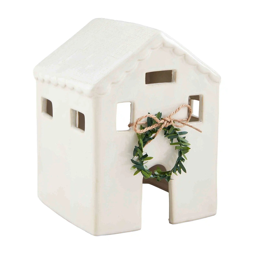 White ceramic Christmas house figurine with a milk glazed finish, arched doorway, and greenery wreath. Available in multiple sizes.