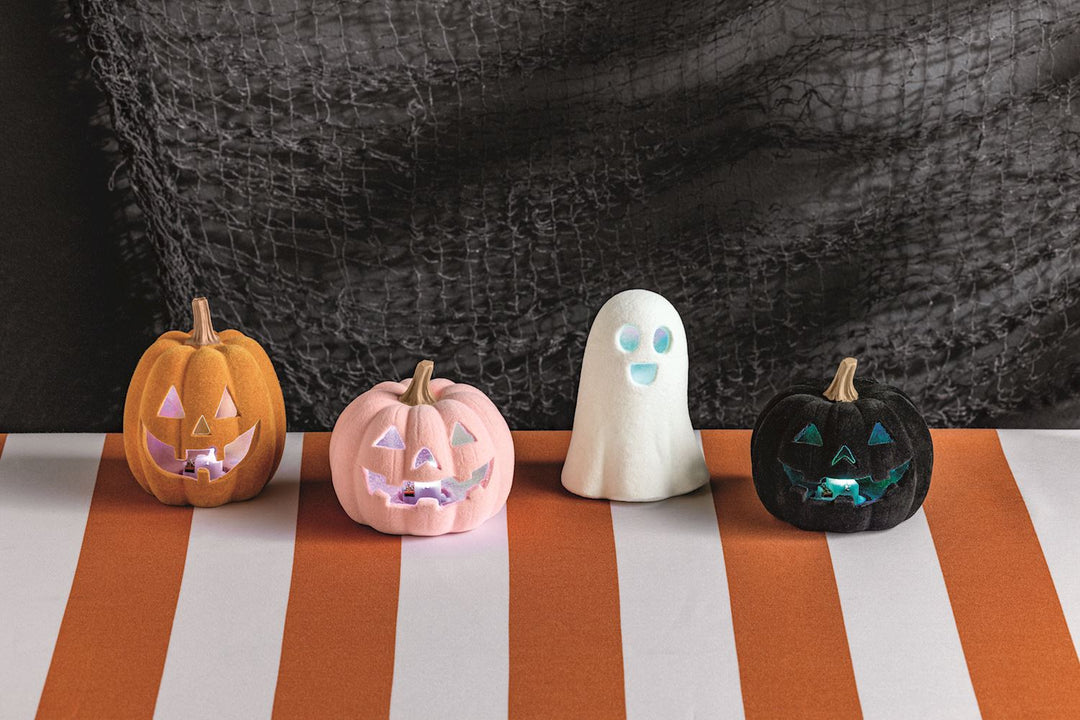 Set of four LED light-up flocked Jack-O-Lantern décor pieces—orange pumpkin, pink pumpkin, black pumpkin, and smiling ghost—with glowing faces. Available in small (6″), medium (8″), and large (10″) sizes.