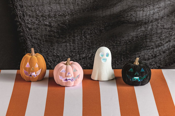 Set of four LED light-up flocked Jack-O-Lantern décor pieces—orange pumpkin, pink pumpkin, black pumpkin, and smiling ghost—with glowing faces. Available in small (6″), medium (8″), and large (10″) sizes.