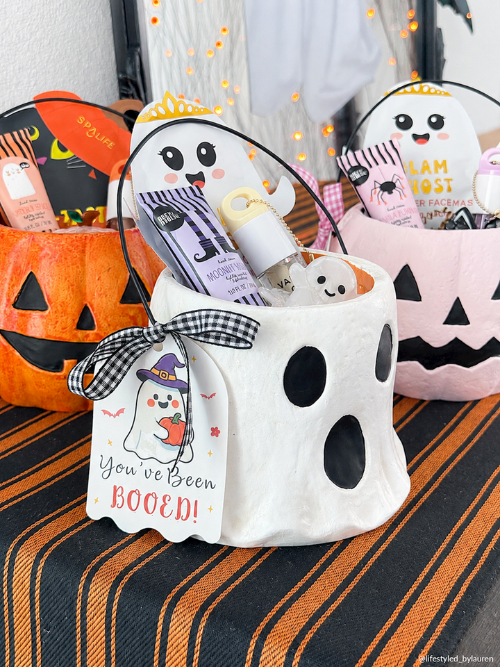White ghost-shaped bucket with black eyes, filled with Halloween treats and topped with a “You’ve Been Booed!” tag. Available in mini size.