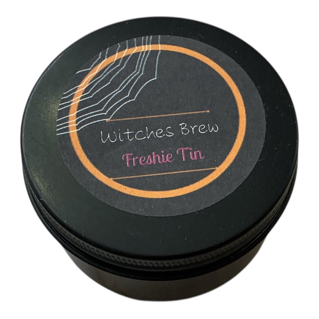 Round black Freshie Tin labeled "Witches Brew" with spiderweb design, orange-pink text; available in multiple sizes.
