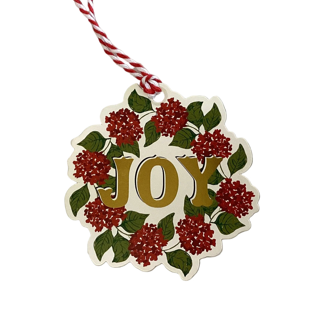 Gift Tag Book die-cut holiday gift tag featuring a red flower and green leaf wreath with gold “JOY” text on red and white baker’s twine.