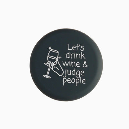 Round black Wine Cap with white hand holding wine glass, "Let's drink wine & judge people" text. Available in multiple sizes.