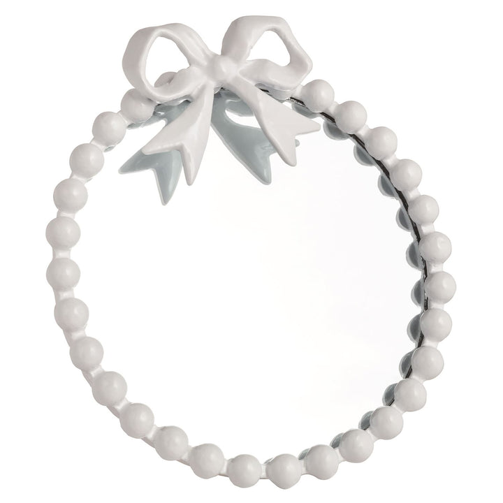 Round mirror with white beaded frame and metal bow on top; available in 12" and 18" diameters.