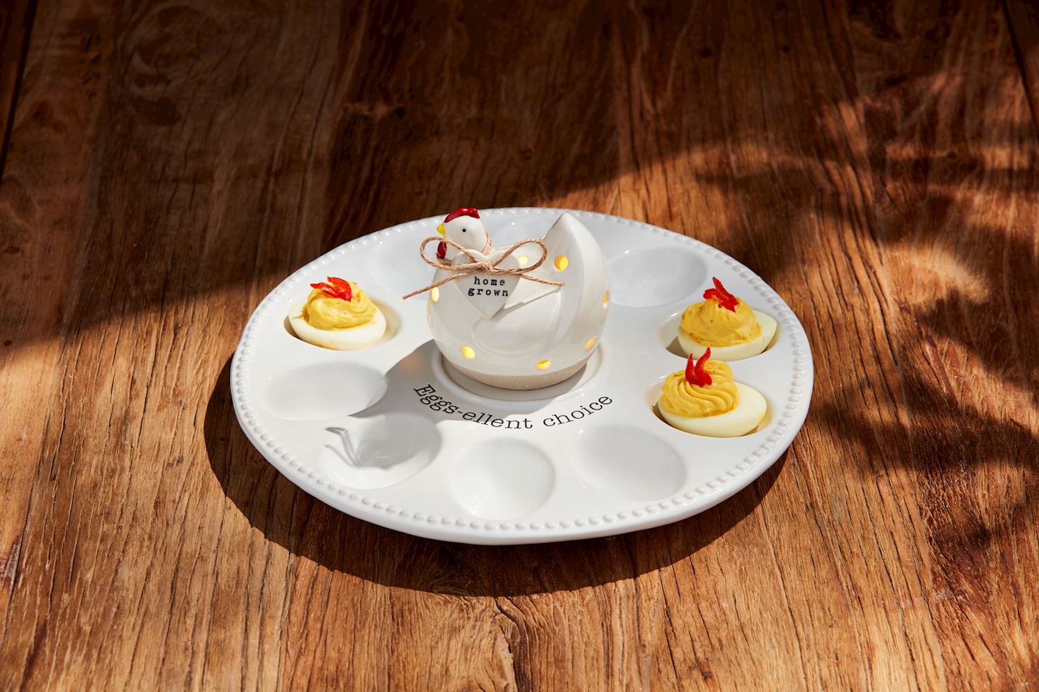 The Deviled Egg Tray Light-Up Holder stylishly holds four stuffed eggs. It features a hen-shaped salt shaker labeled "home grown" in the center.